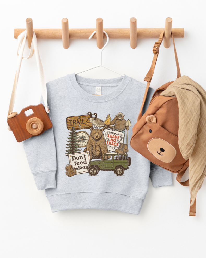 Children's sweatshirt with bear and truck design, hanging on a wooden rack with accessories.