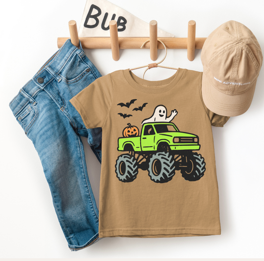 Children's brown t-shirt with green monster truck graphic, blue jeans, beige cap, and wooden hanger on white background
